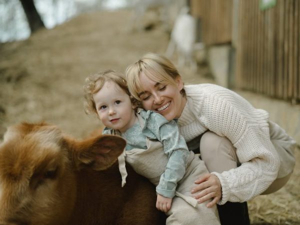 A mother and child enjoy a tender moment with a cow outdoors, embracing nature's warmth.